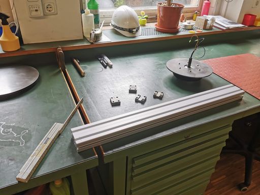 Four metal brackets, an aluminium extrusion, a folding ruler and one flanged wheel on a workbench