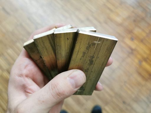 A hand holding four small brass plates